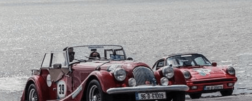 Two classic cars parked near a body of water