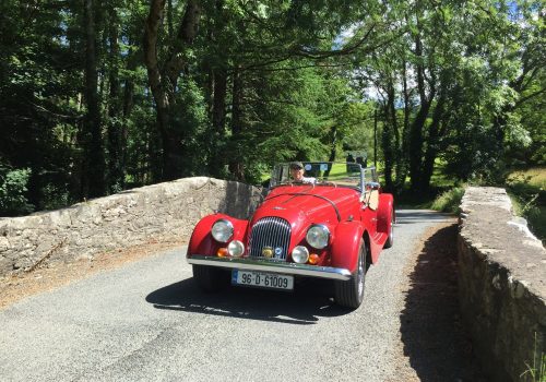 Red classic car driving over a stone bridge in nature