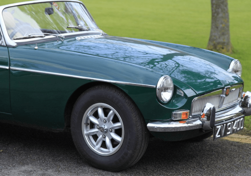 Green classic car parked on a road with grass in background