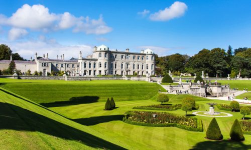 Lush green gardens and a grand estate under a blue sky