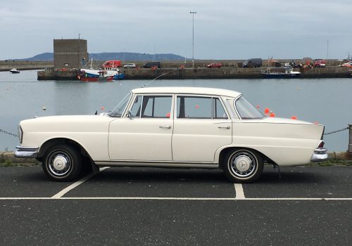 White Mercedes 230S Fintail parked by the water