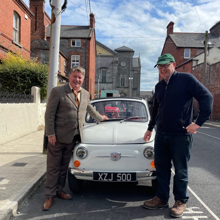 Two men standing beside a classic white car on a street