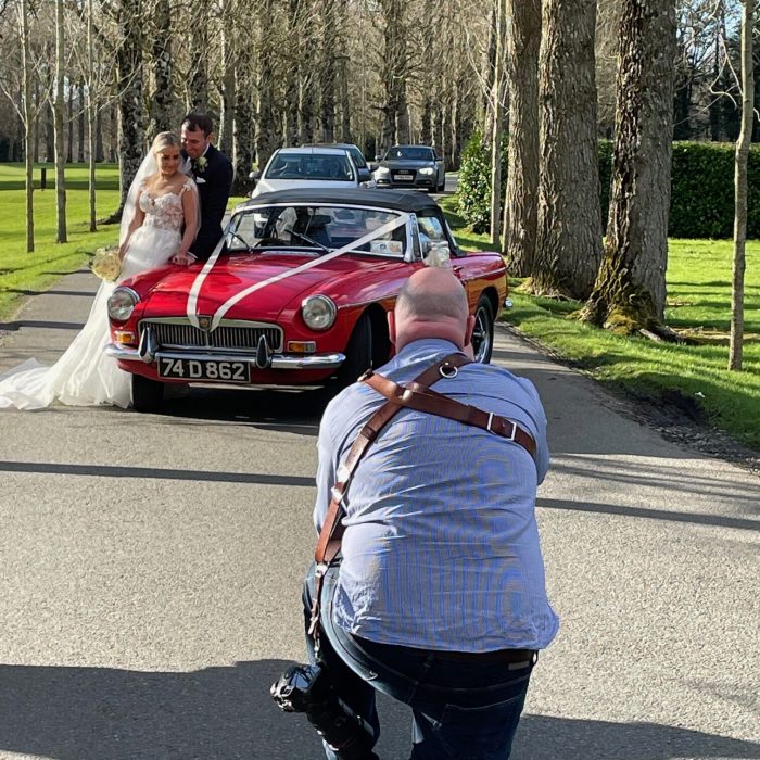 Couple posing by a classic red car during a photoshoot